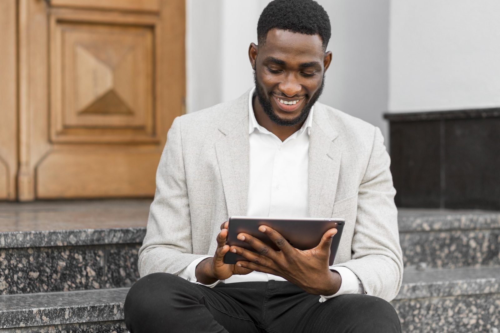 Un lecteur consulte un ebook sur sa tablette, assis sur des marches.